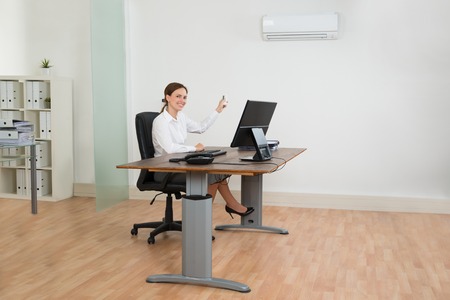 44713156 - young businesswoman sitting on chair using air conditioner in office